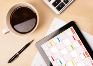 desktop with coffee cup, pen, calculator, and a tablet showing a calendar on its screen