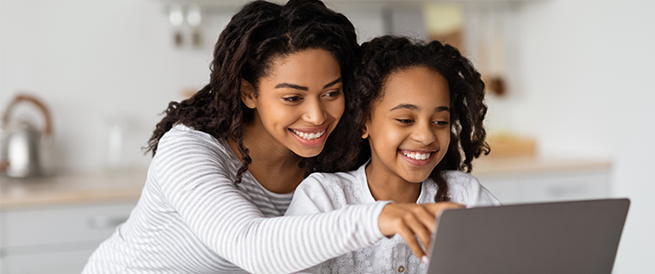 Smiling mother and daughter sitting together with laptop