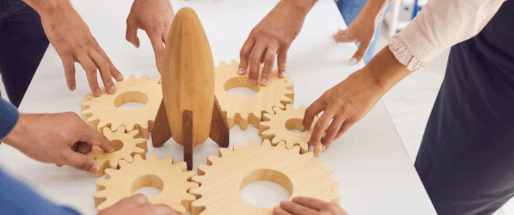business people around a table arranging wooden gears around a rocket