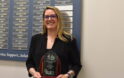 Dr. Caitlin Bennyhoff with Annie Sullivan Award in front of list of previous recipients.