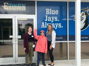 boy smiling and waving in front of two smiling women, next to entrance to Elizabethtown School District building