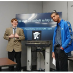two young men standing in front of a television screen showing a slide from their PennDOT Innovations Challenge presentation