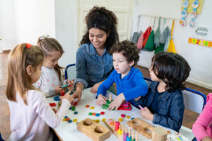 Diverse group of students playing with wooden toys while cheerful teacher supervises - Education concepts