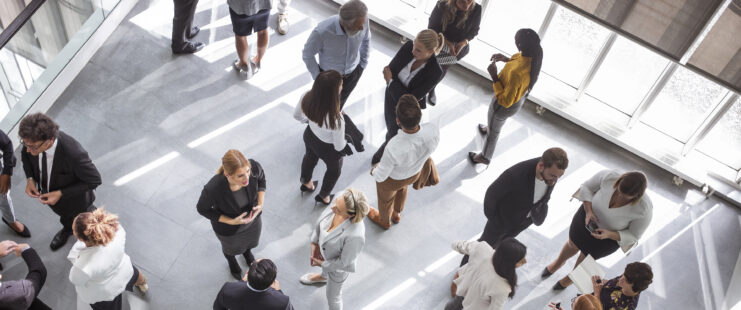 Diverse business professionals engaging at a conference event, dressed in formal business attire, networking and discussing ideas. Set in a modern conference hall, attendees use laptops and notepads for effective communication and collaboration.