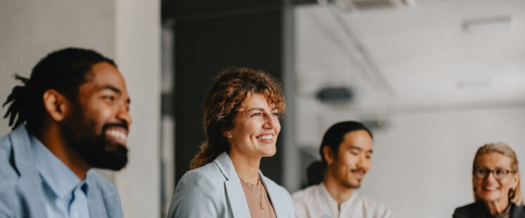 Diverse group of smiling colleagues in a business meeting, collaborating and discussing ideas in a modern office setting.