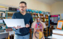 Male tearcher using laptop to learn about human anatomy model.