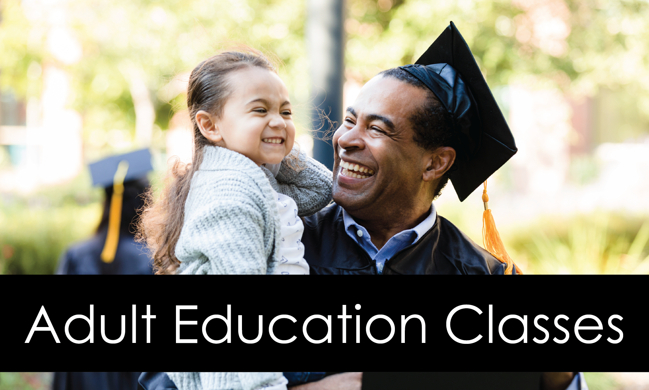 Older graduate smiling with smiling child in his arms.